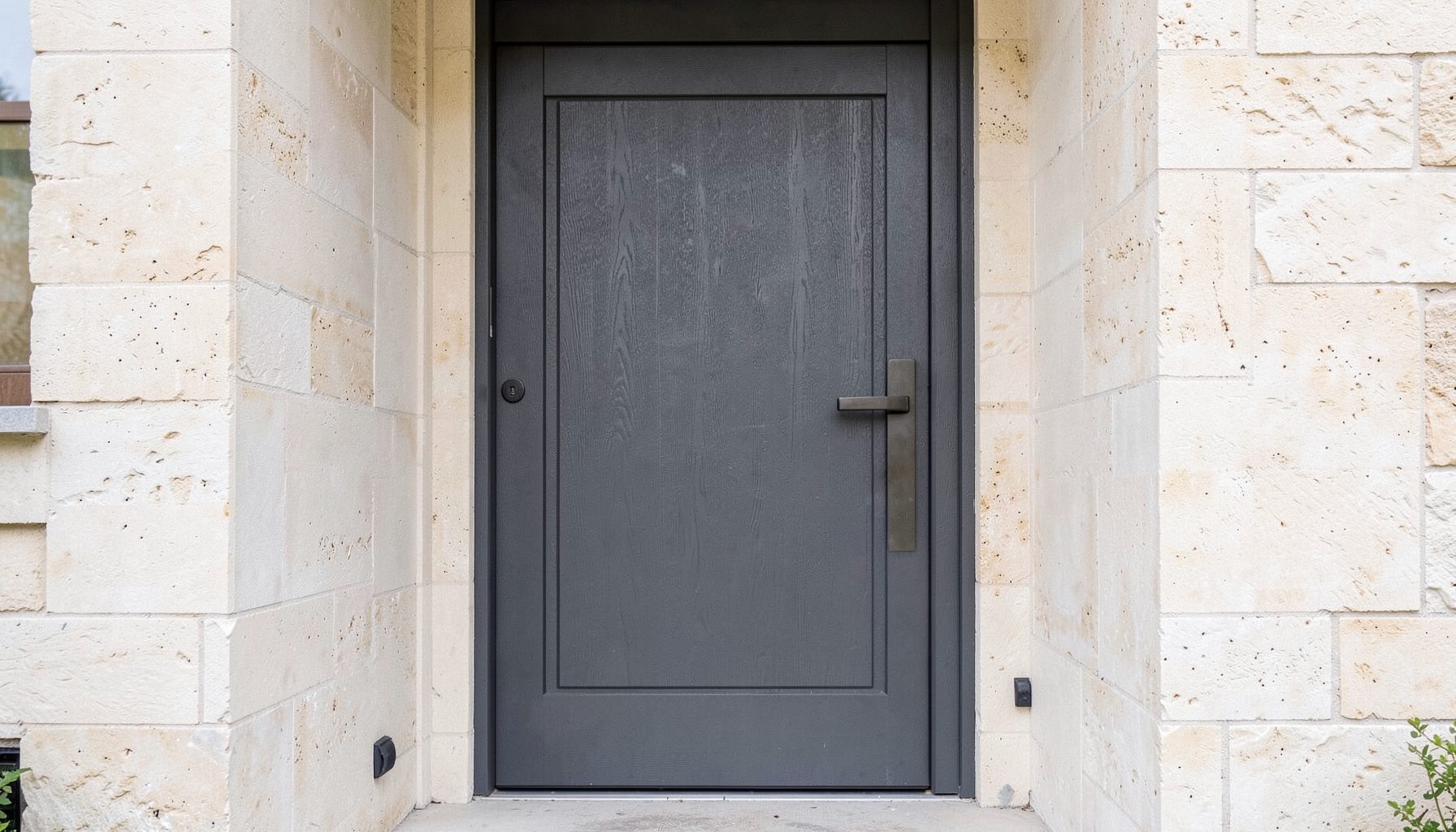 A sturdy composite front door in deep grey with a textured finish, set in a light stone doorway, conveying a calm, secure and modern residential mood