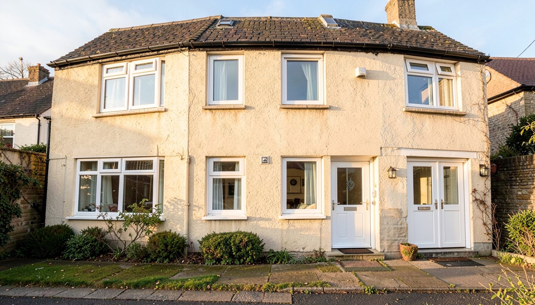 Five white UPVC windows and two doors on a modern Scottish semi-detached house, warm afternoon light, tidy suburban setting