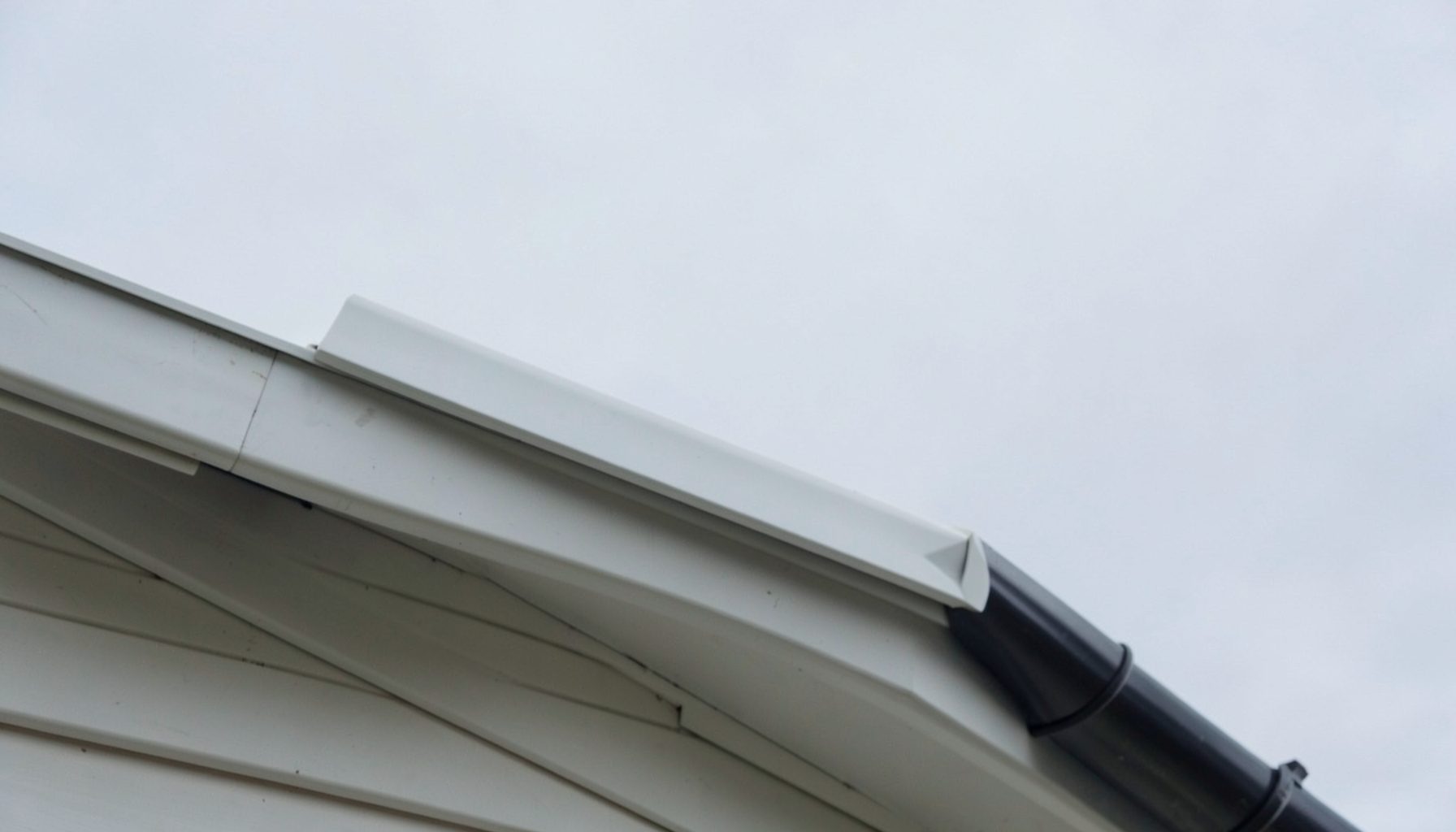 A close-up view along a pristine white UPVC roofline with a dark gutter against a pale grey overcast sky, showing clean lines and no visible wear