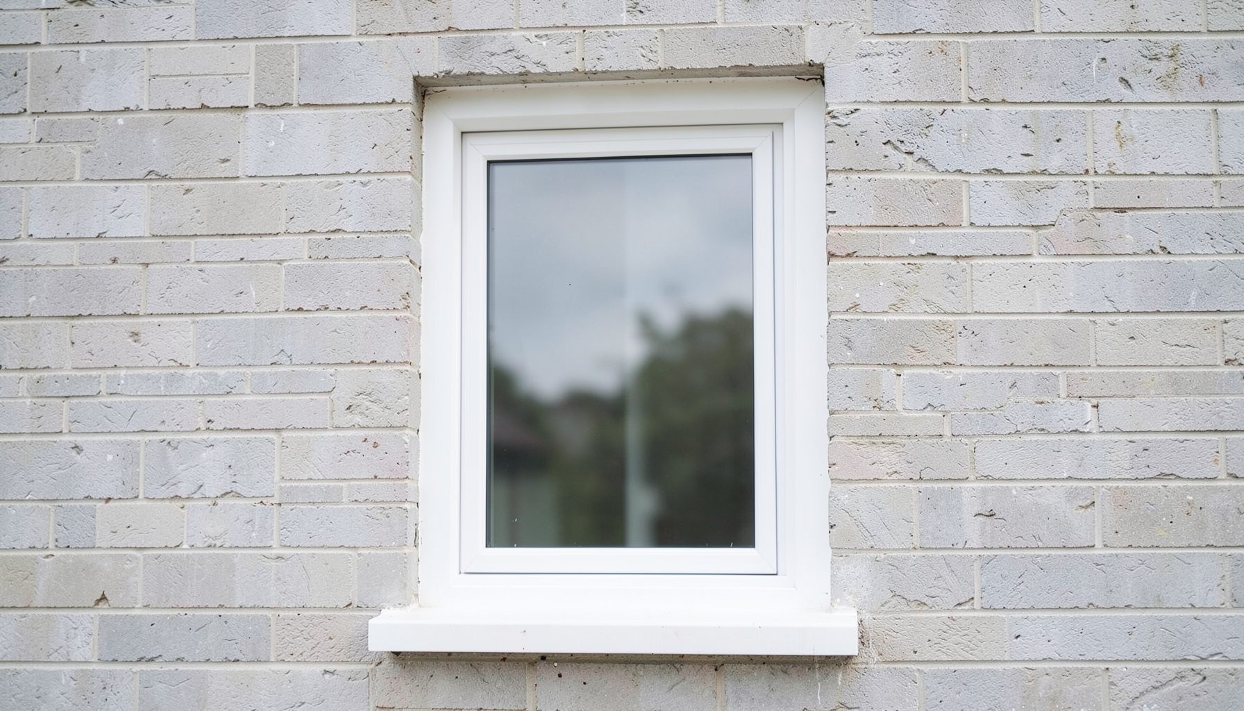 Close view of a white UPVC casement window with clean straight frames, set into a pale grey brick wall, calm and tidy residential mood