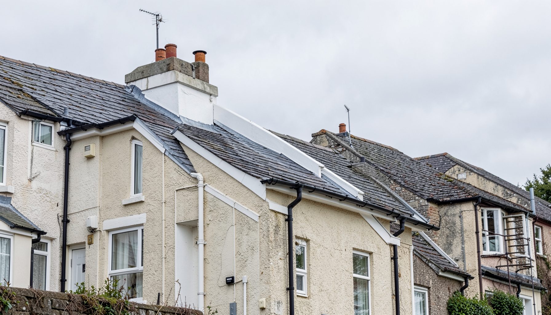 A row of terraced houses under a soft grey Scottish sky, with clean white roofline fascias and dark guttering catching the muted daylight